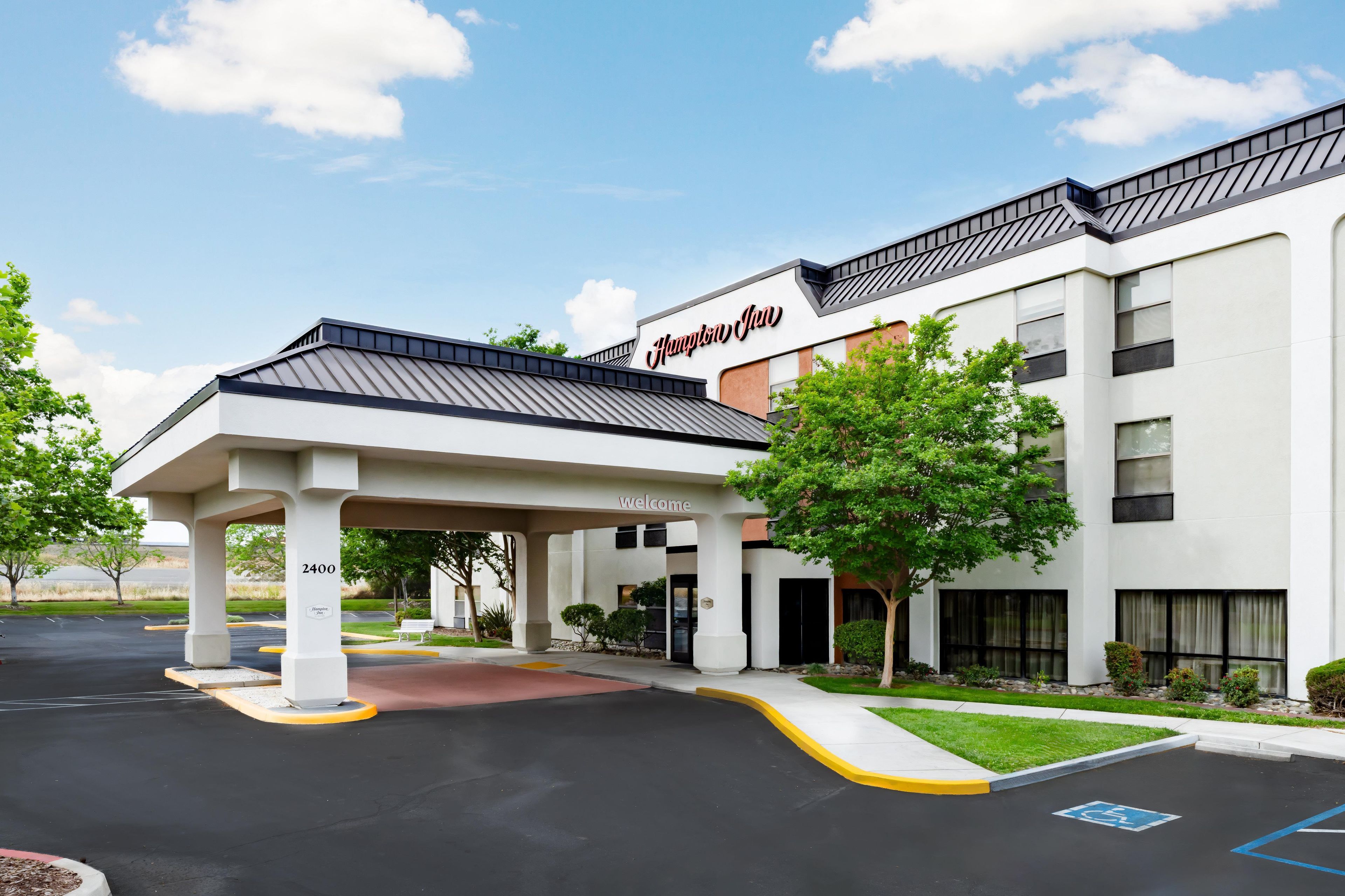 A Hampton Inn with a covered entrance, a parking lot, and a clear sky.