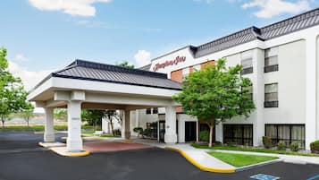A Hampton Inn with a covered entrance, a parking lot, and a clear sky.