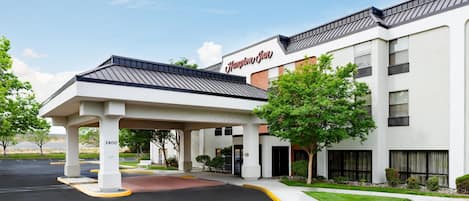 Un Hampton Inn con entrada techada, estacionamiento y cielo despejado.