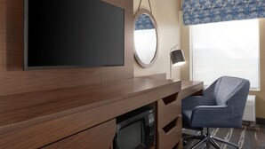 A hotel room with a flat-screen TV mounted on the wall, a round mirror, a desk with a microwave, and a chair. - Hampton Inn Tracy (Tracy)