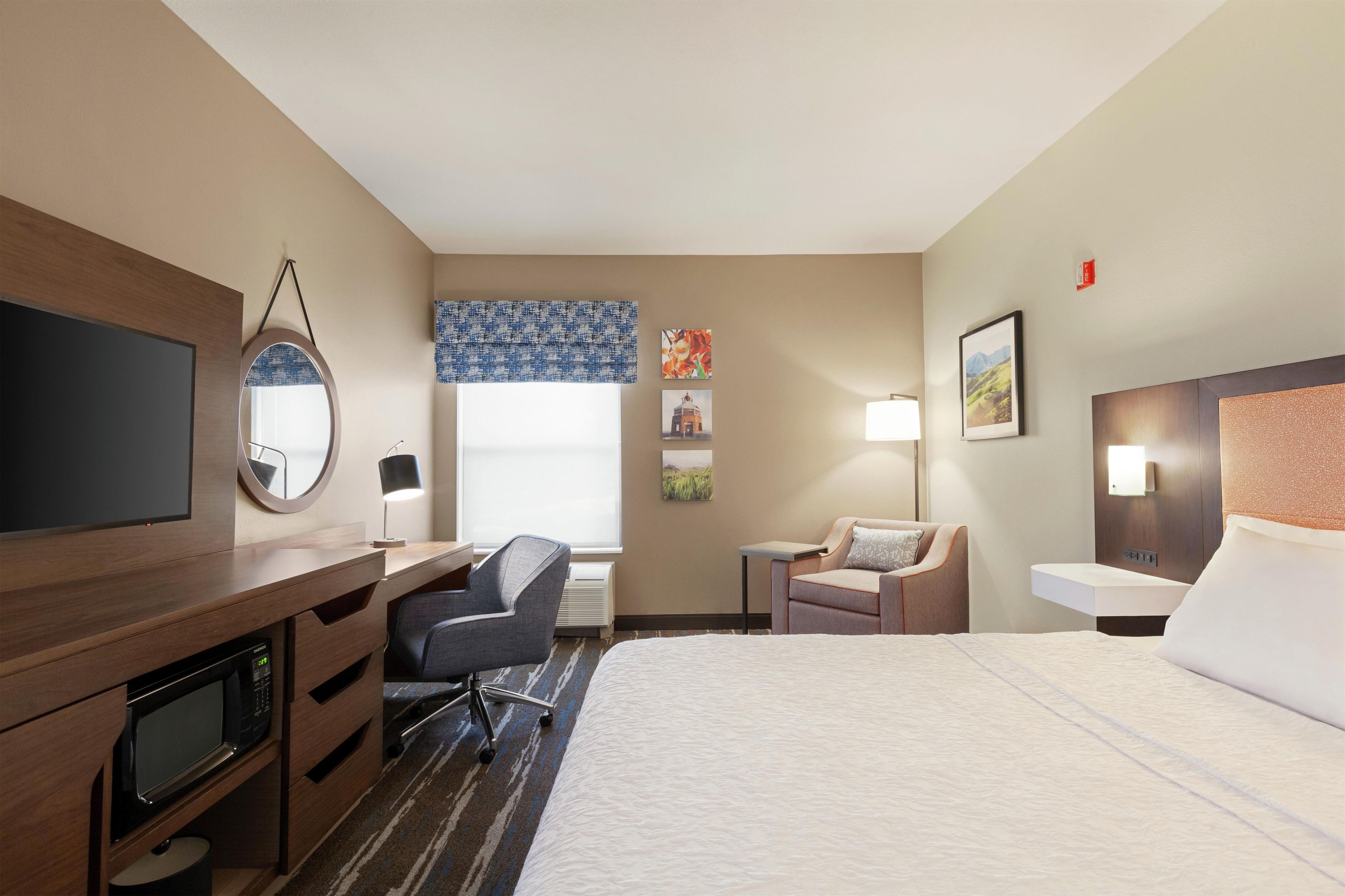 Habitación de hotel con cama, escritorio, silla, televisor y obras de arte en las paredes.