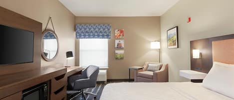 Habitación de hotel con cama, escritorio, silla, televisor y obras de arte en las paredes.