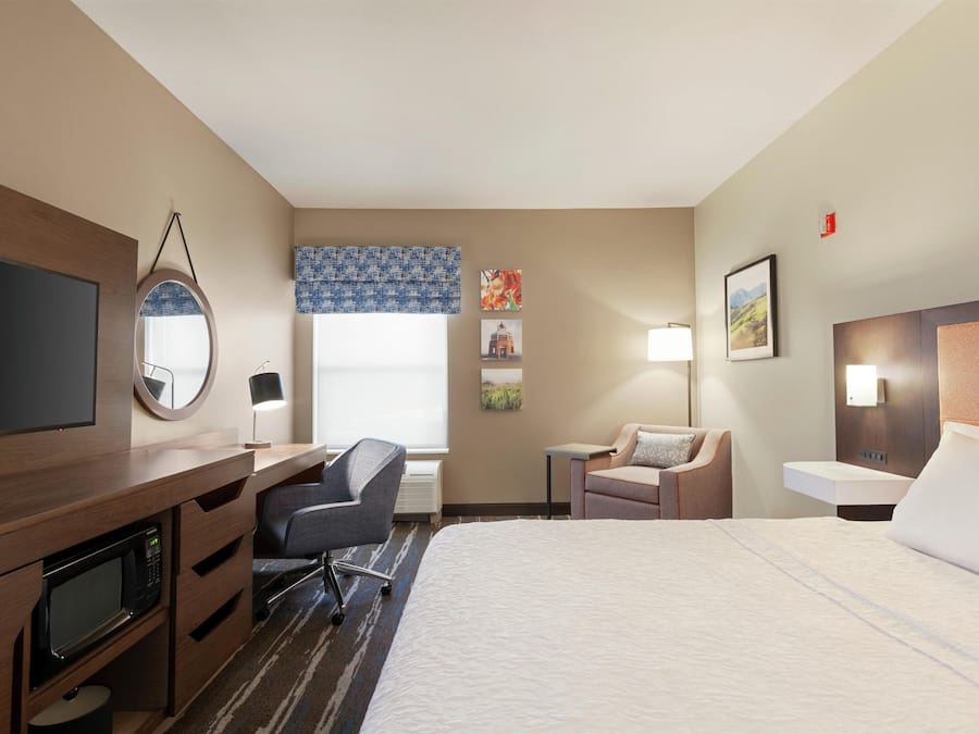 A hotel room with a bed, desk, chair, television, and artwork on the walls.