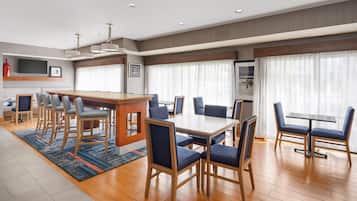 A modern hotel room with a dining area, a kitchen, and a large window with curtains.