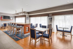 Una habitación de hotel moderna con comedor, cocina y un amplio ventanal con cortinas.