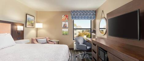 Ein Hotelzimmer mit einem großen Bett, einem Schreibtisch mit Stuhl, einem Fernseher und einem Fenster mit Blick auf Gebäude.