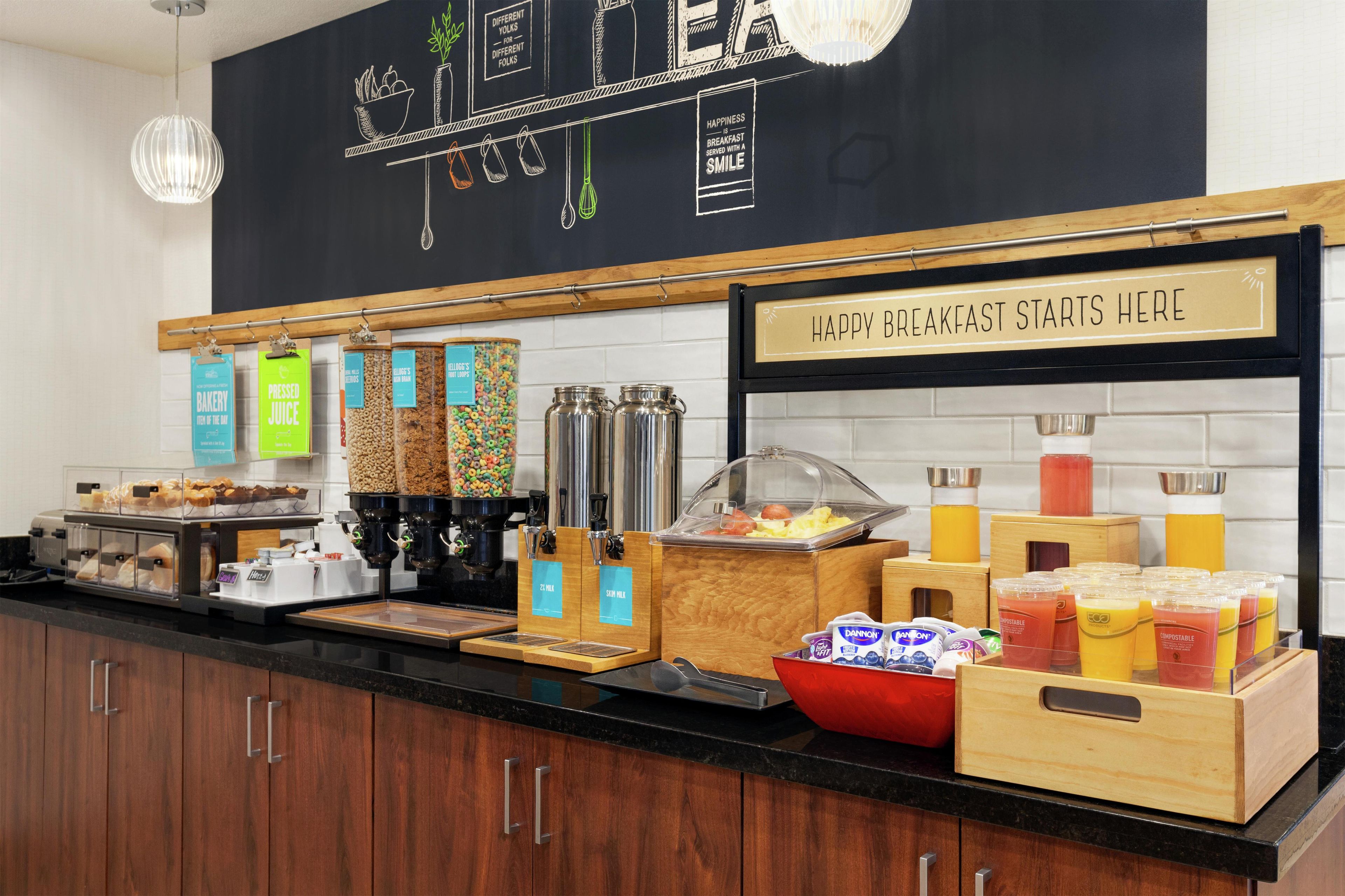 A breakfast buffet area with various food options and a sign indicating breakfast starts here.