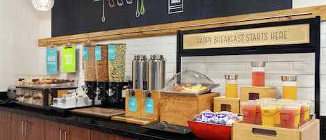 A breakfast buffet area with various food options and a sign indicating breakfast starts here.