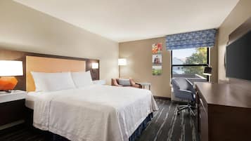 A hotel room with a large bed, a desk, a chair, a TV, and a window with a view.
