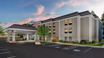A modern hotel with a covered entrance, a sign reading 'Hampton Inn,' and a parking lot with marked spaces.