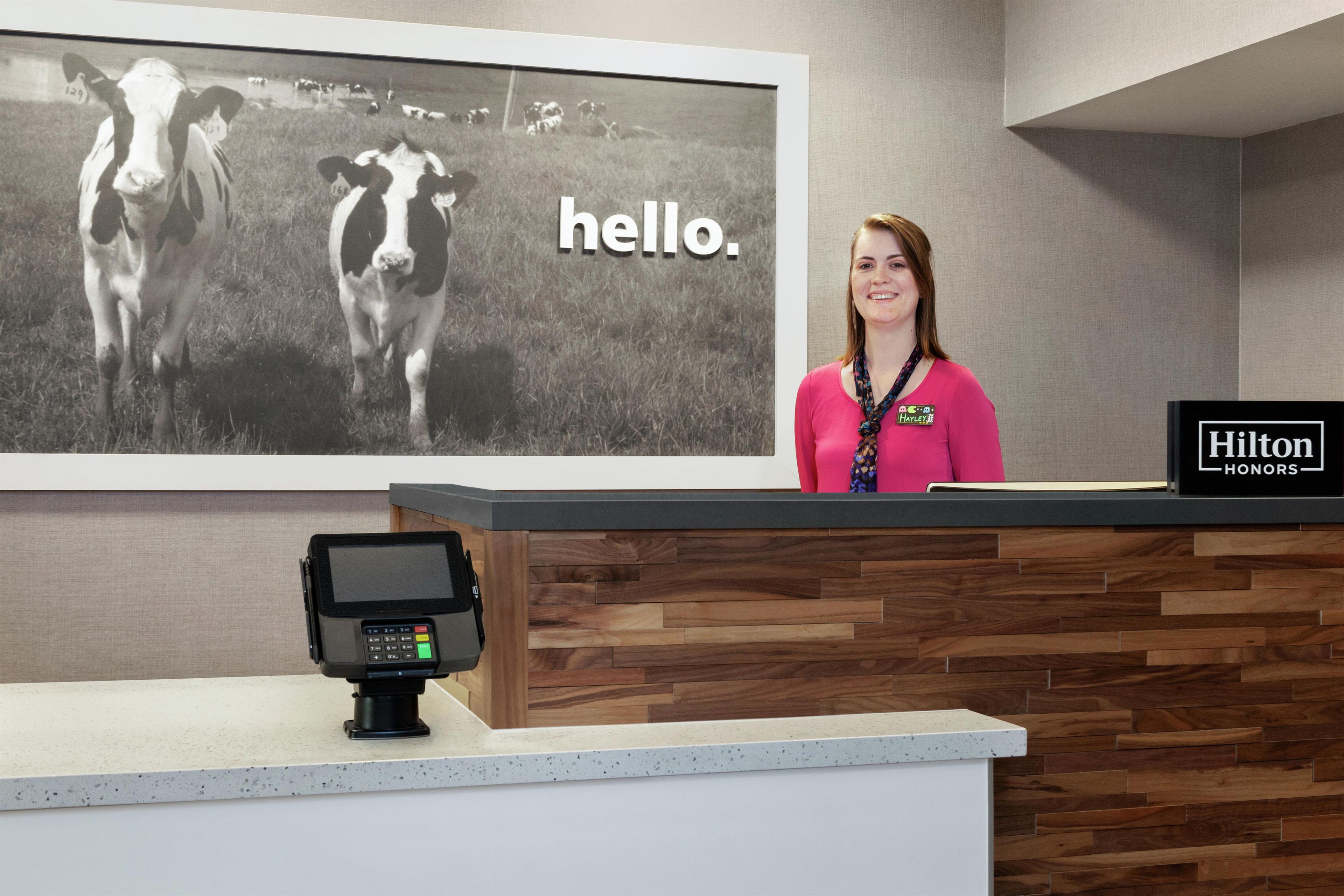 A hotel reception desk with a large black and white photo of cows and the word 'hello.'