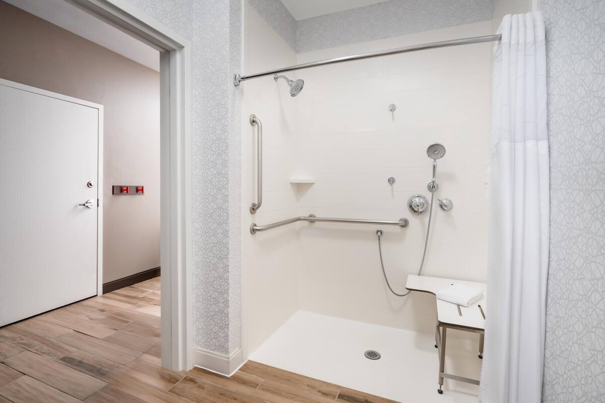 A modern bathroom with a walk-in shower, a handrail, a handheld showerhead, and a small sink.