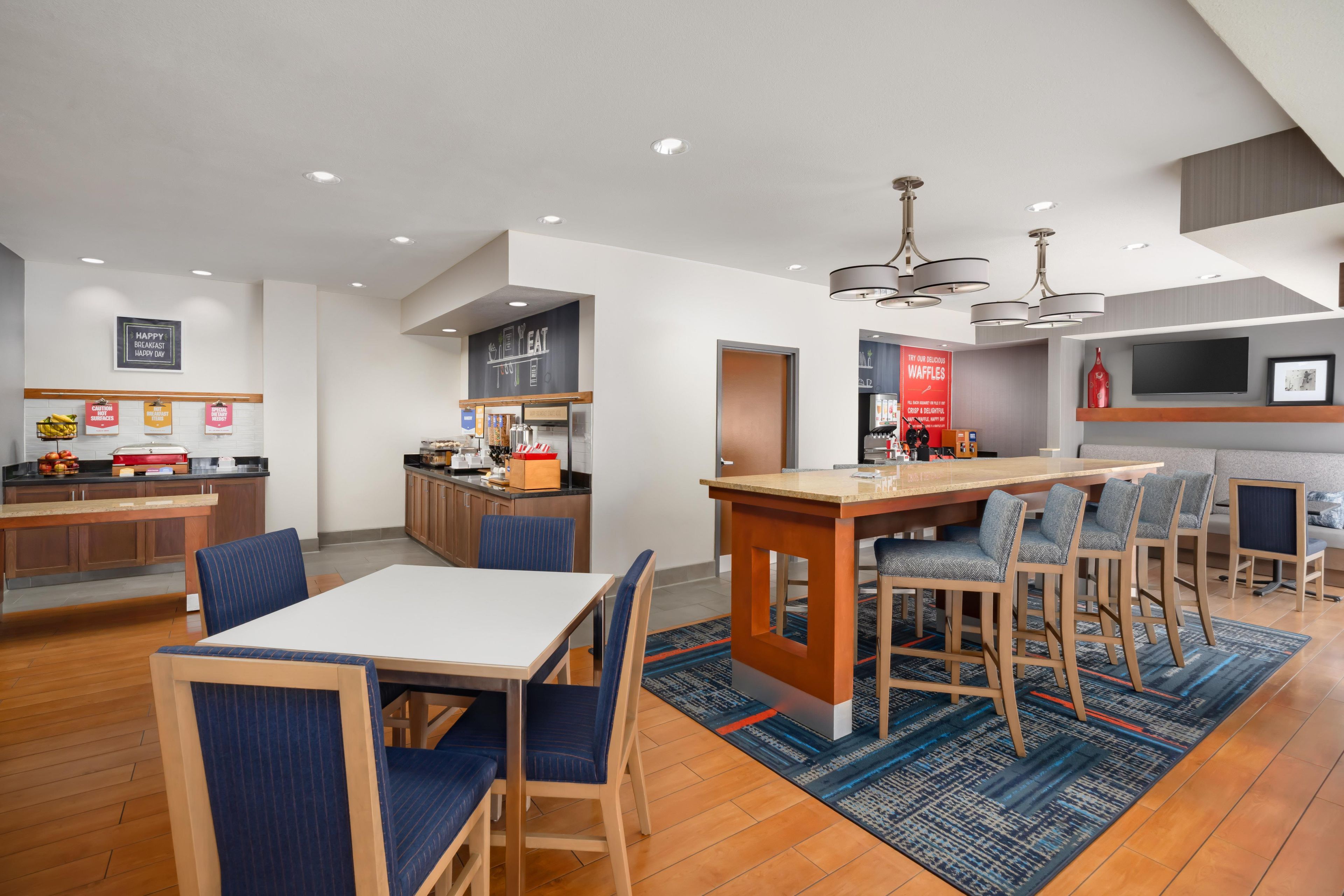 A modern kitchen with a central island, bar seating, and a dining area with blue upholstered chairs.