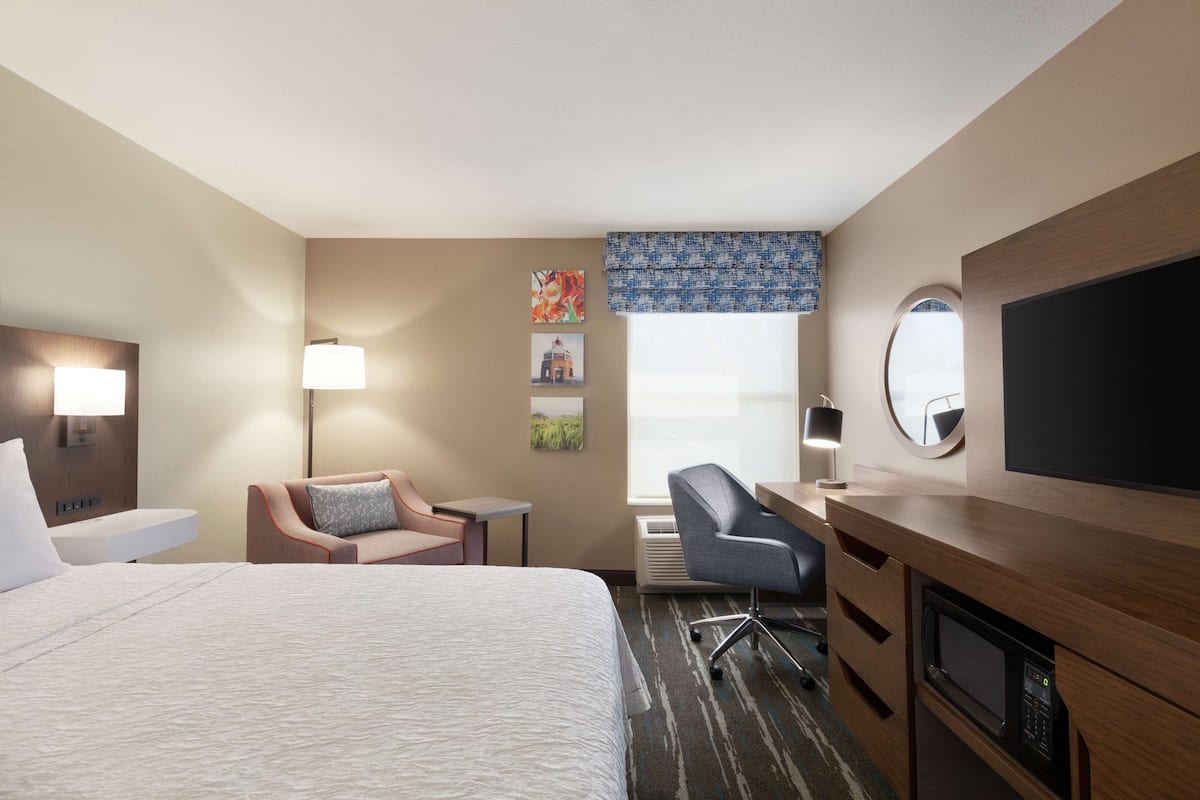A hotel room with a bed, a desk, a chair, a TV, and a microwave.