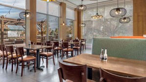 A restaurant with wooden tables and chairs, large windows, and hanging pendant lights.