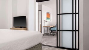 A hotel room with a bed, a flat-screen TV on a wooden stand, a desk with a chair, and a sliding door with frosted glass panels.