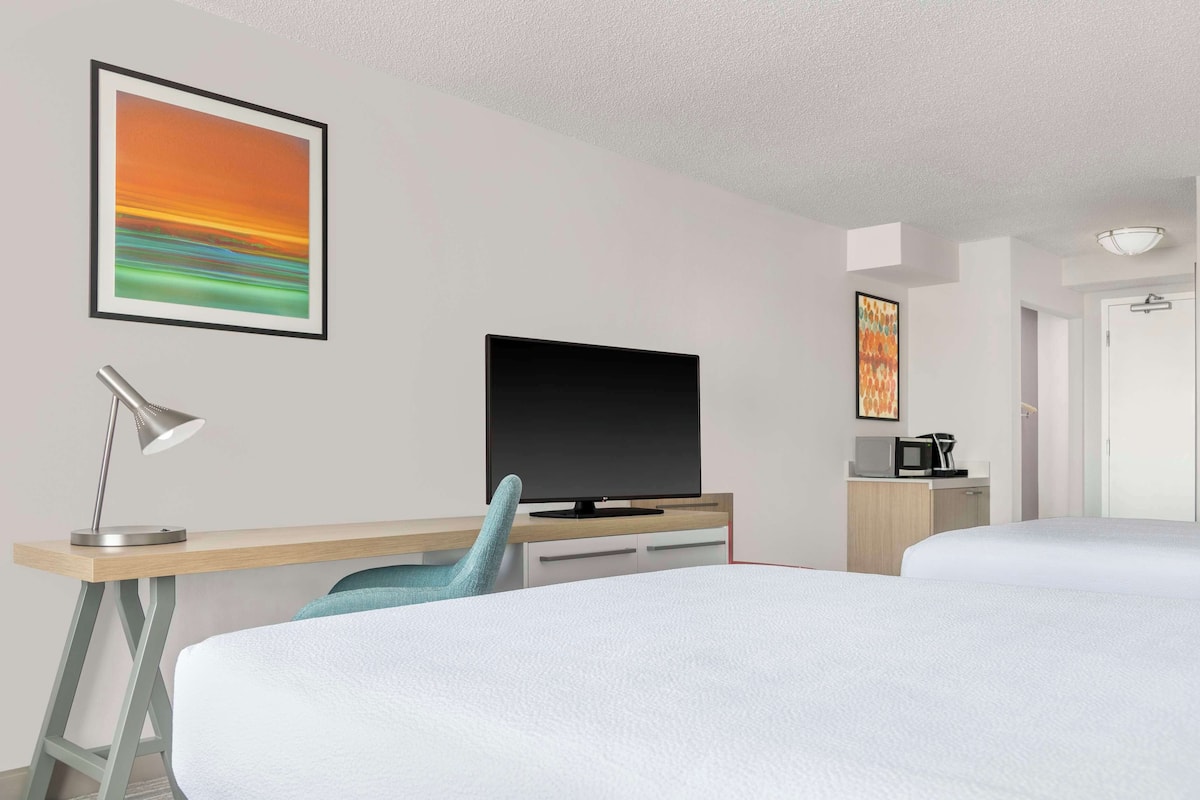 A hotel room with a bed, a desk with a computer monitor, a lamp, a chair, and a television.