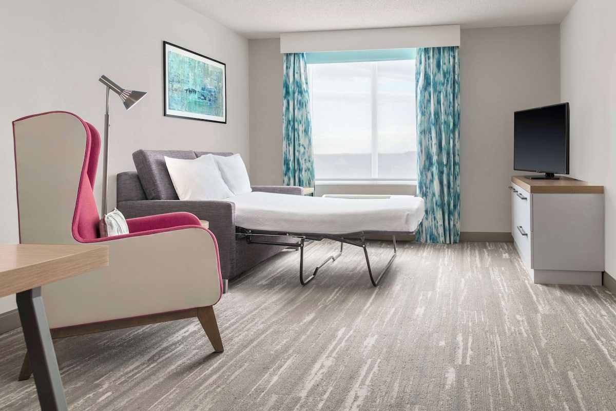 A hotel room with a bed, a desk, a chair, a TV, and a window with curtains.