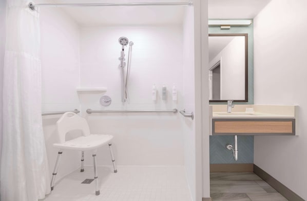 A modern bathroom with a shower, a wheelchair-accessible bench, a sink, and a mirror.