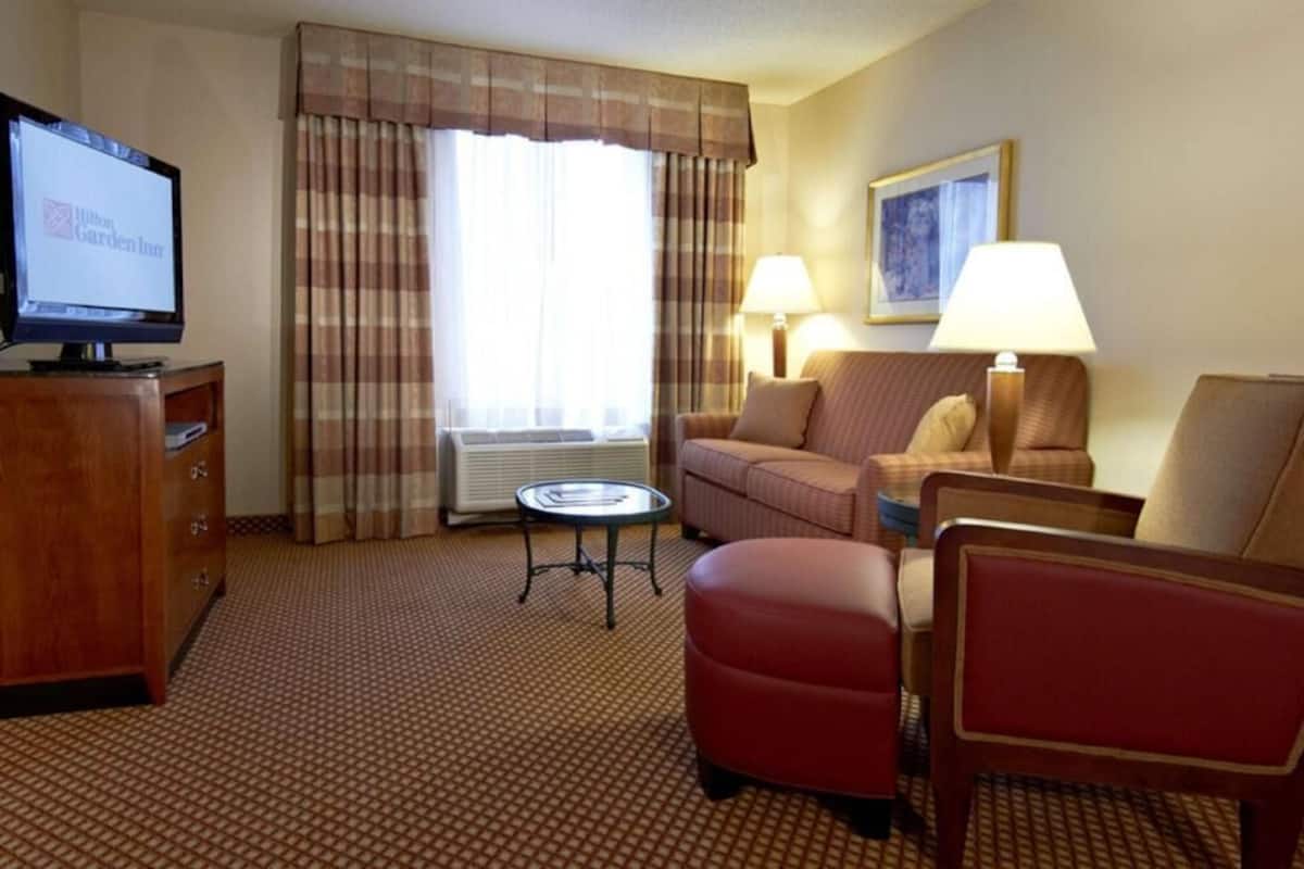 A hotel room with a television, a sofa, a chair, a small table, and a lamp.