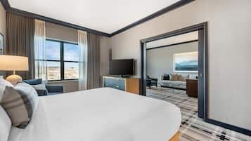 Ein Hotelzimmer mit einem großen Bett, einem Fernseher, einem Schreibtisch und Blick auf die Stadt.