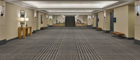 A spacious hotel lobby with a patterned carpet, wooden benches, a reception desk, and a staircase leading to an upper floor.