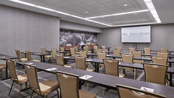A conference room with multiple tables and chairs, a large screen displaying 'OMNI Hotels & Resorts Interlocken | Denver', and a mountain mural on the wall.