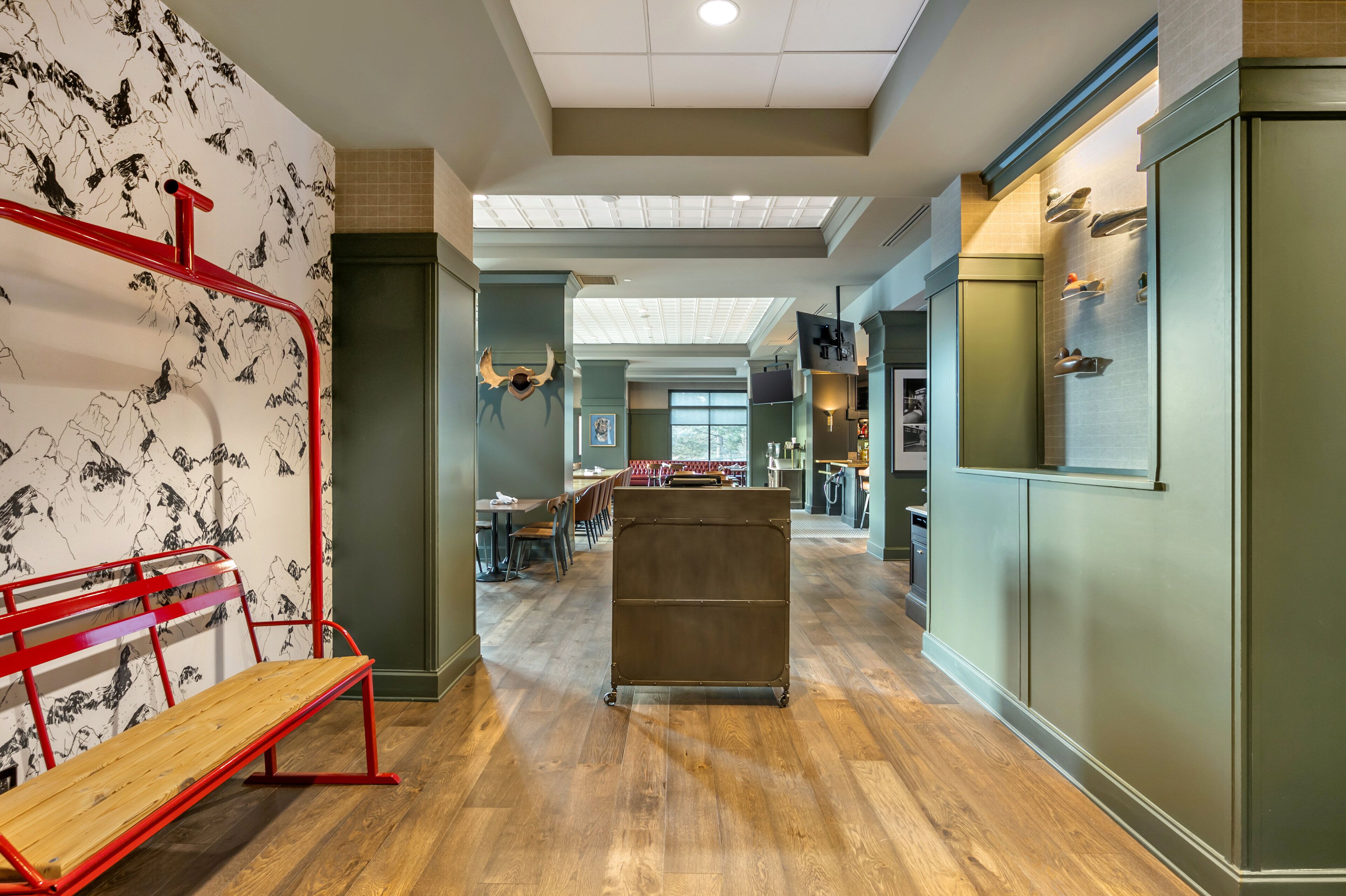 A spacious lobby with a wooden floor, a red bench, a metal cart, and a wall with black and white artwork.