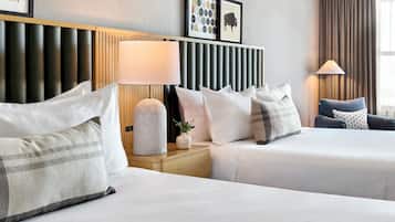 A hotel room with two beds, a wooden headboard, a nightstand with a lamp, and a wall with framed pictures.