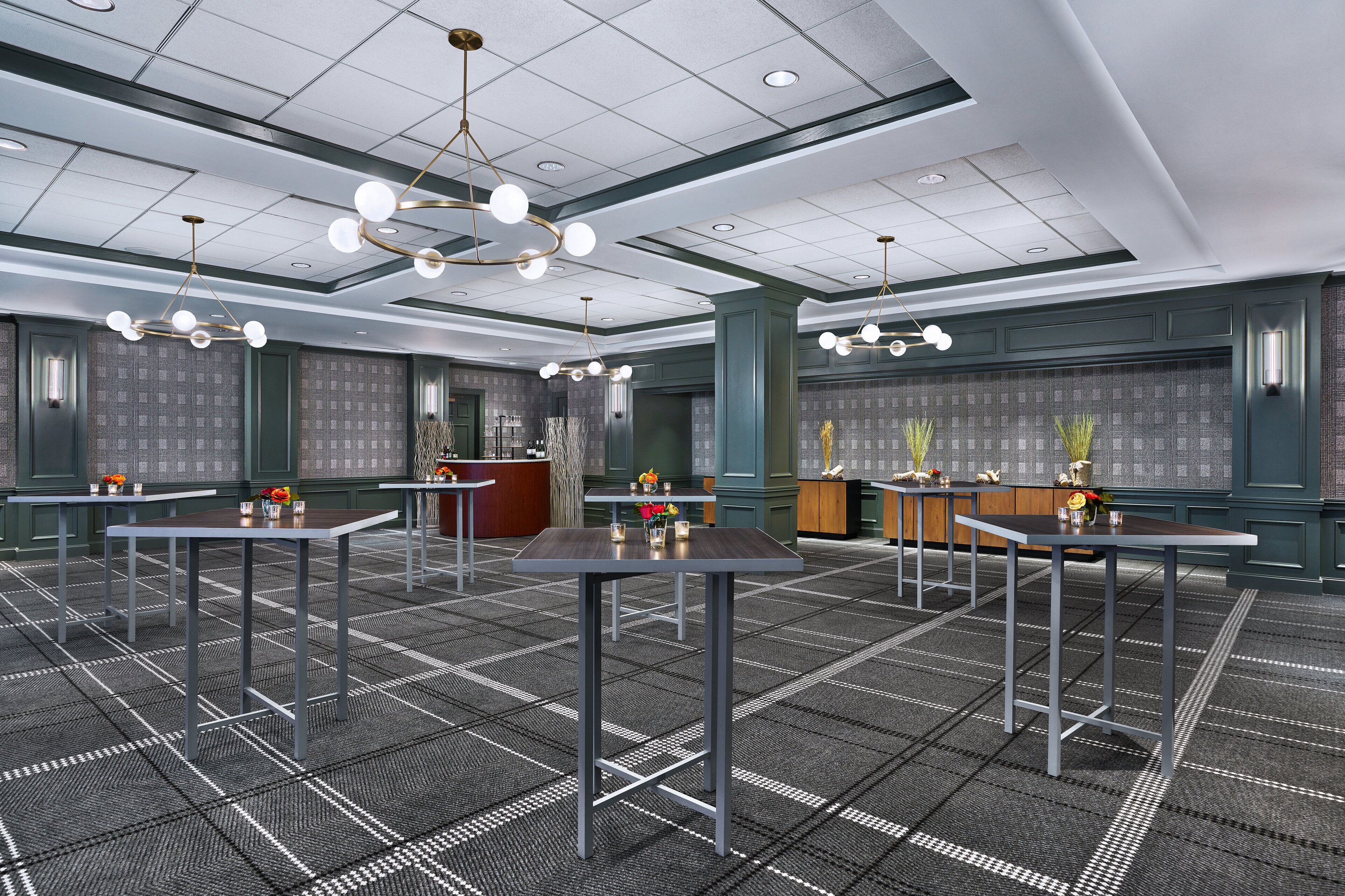 A spacious conference room with multiple tables and chairs, a podium, and decorative plants.