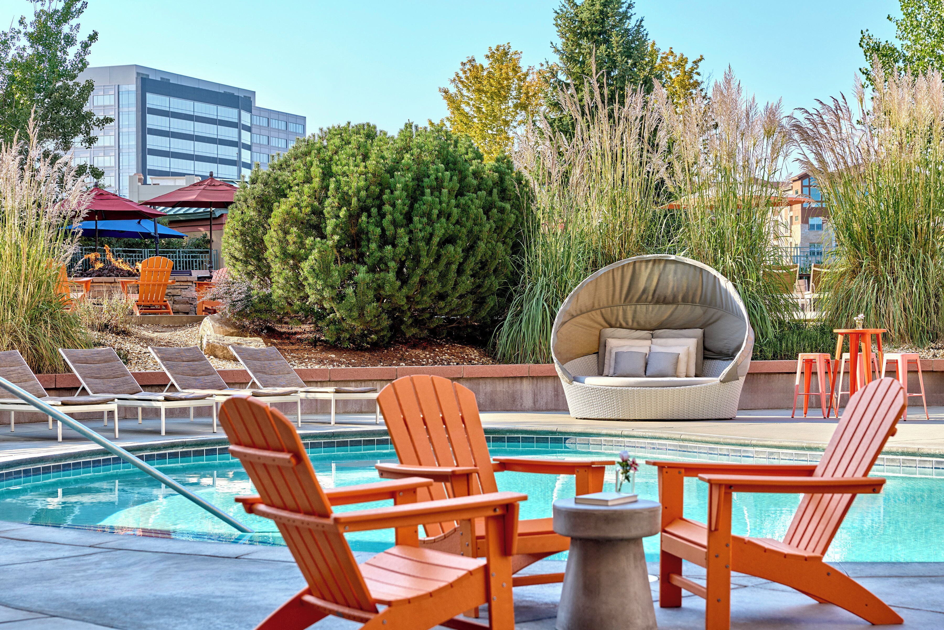 A pool area with Adirondack chairs, a wicker sofa, and a view of a building in the background.