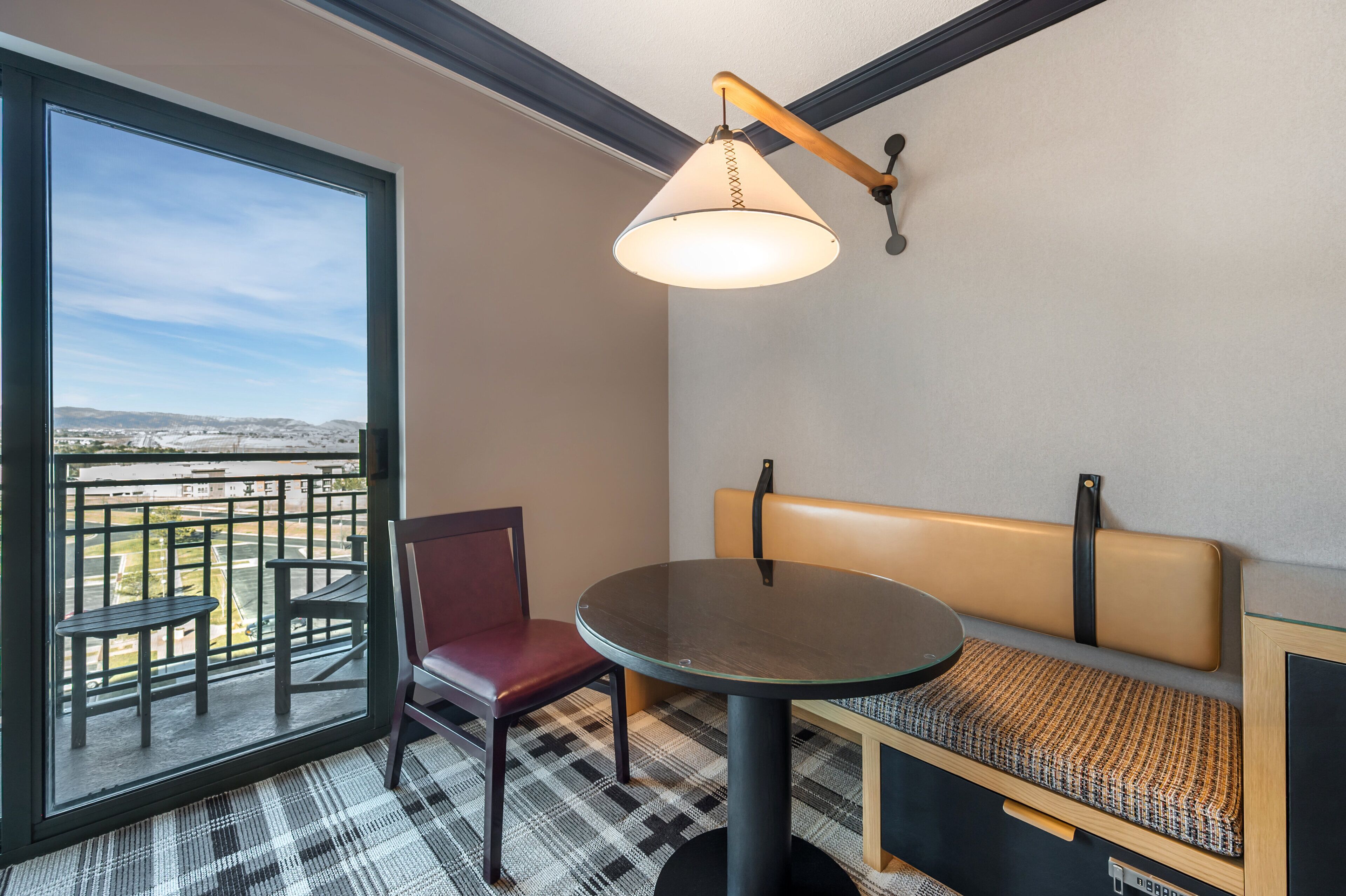 A balcony with a view of a cityscape, a round table, a bench, and a chair.