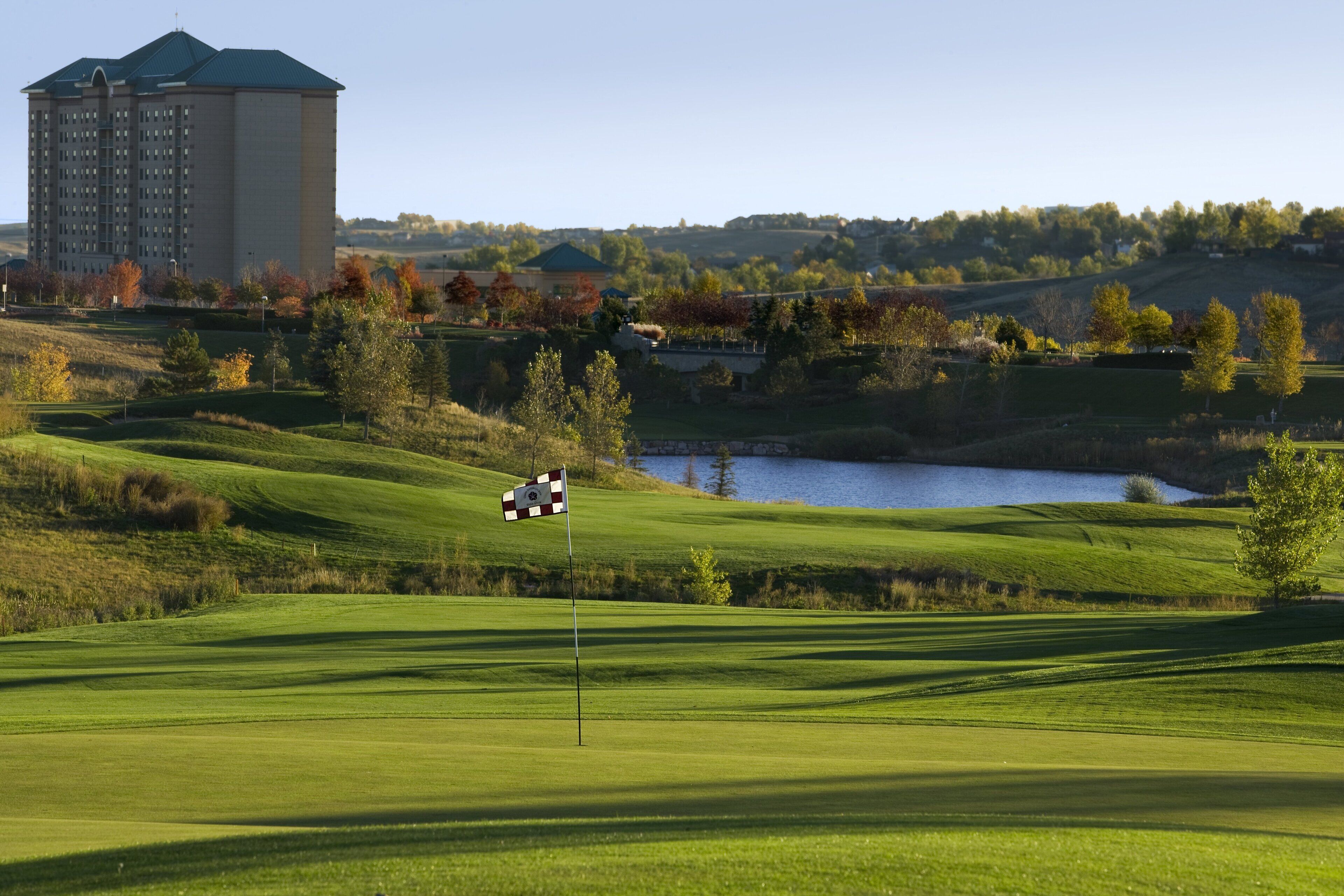 A golf course with a flagstick, a building in the background, and a body of water.