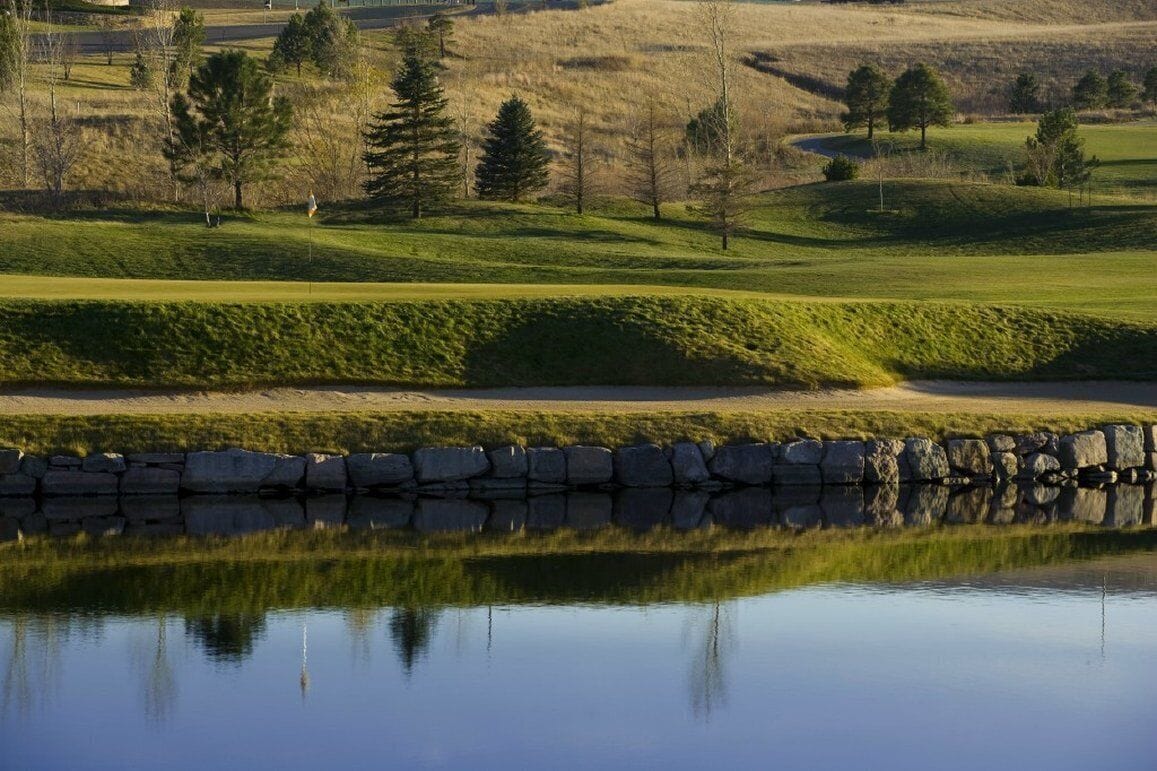Un parcours de golf avec un étang, un mur de pierres et des arbres.