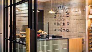 L’intérieur d’un café présente un comptoir où sont exposées des pâtisseries, un mur orné d’une enseigne représentant du café et des produits divers, et une étagère en bois où sont disposés différents articles.