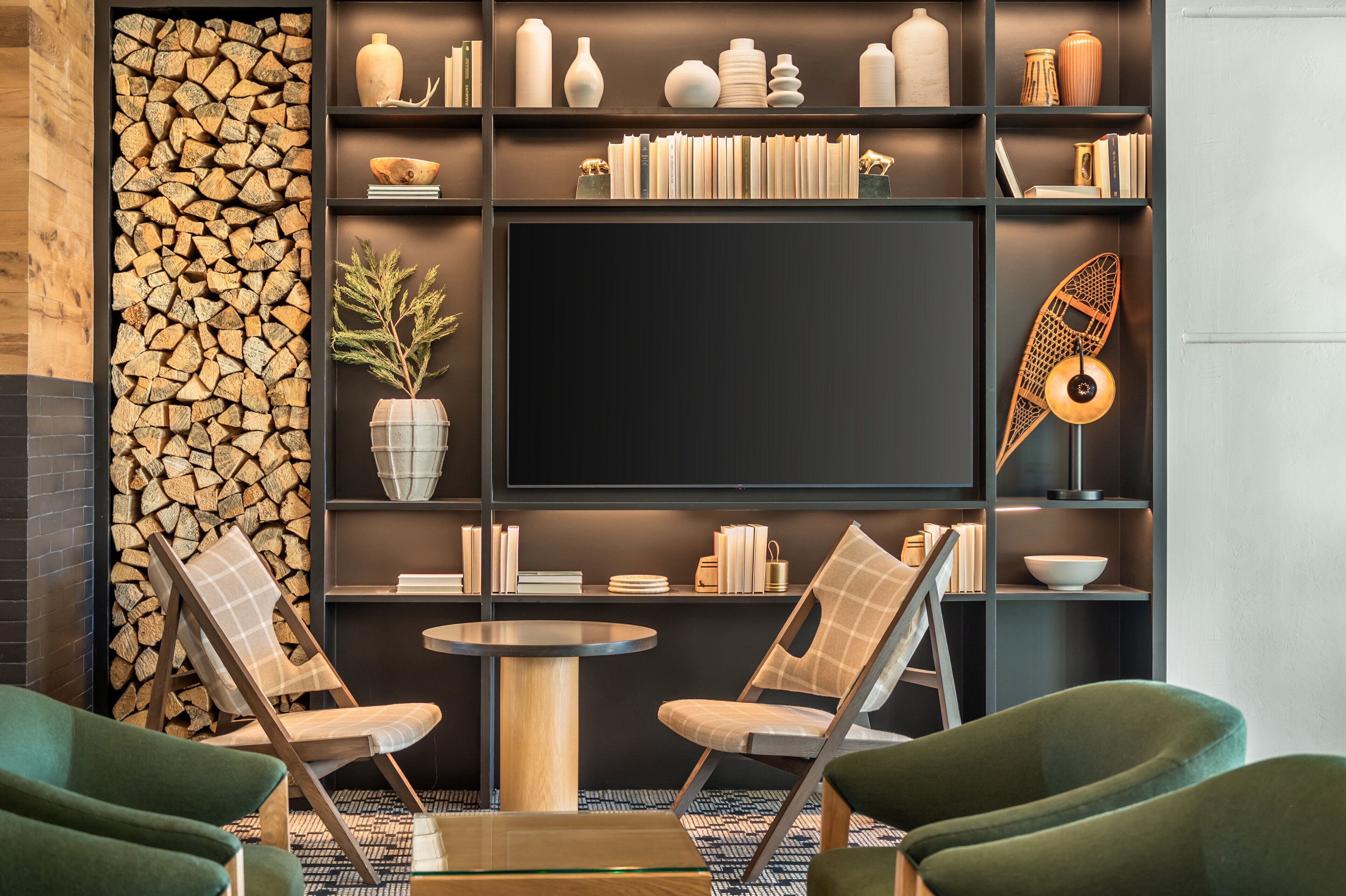 Una sala de estar moderna con chimenea, estanterías, un televisor de pantalla plana y sillones tapizados en tono verde.