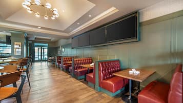 A restaurant interior with wooden flooring, red leather booths, and a modern chandelier.