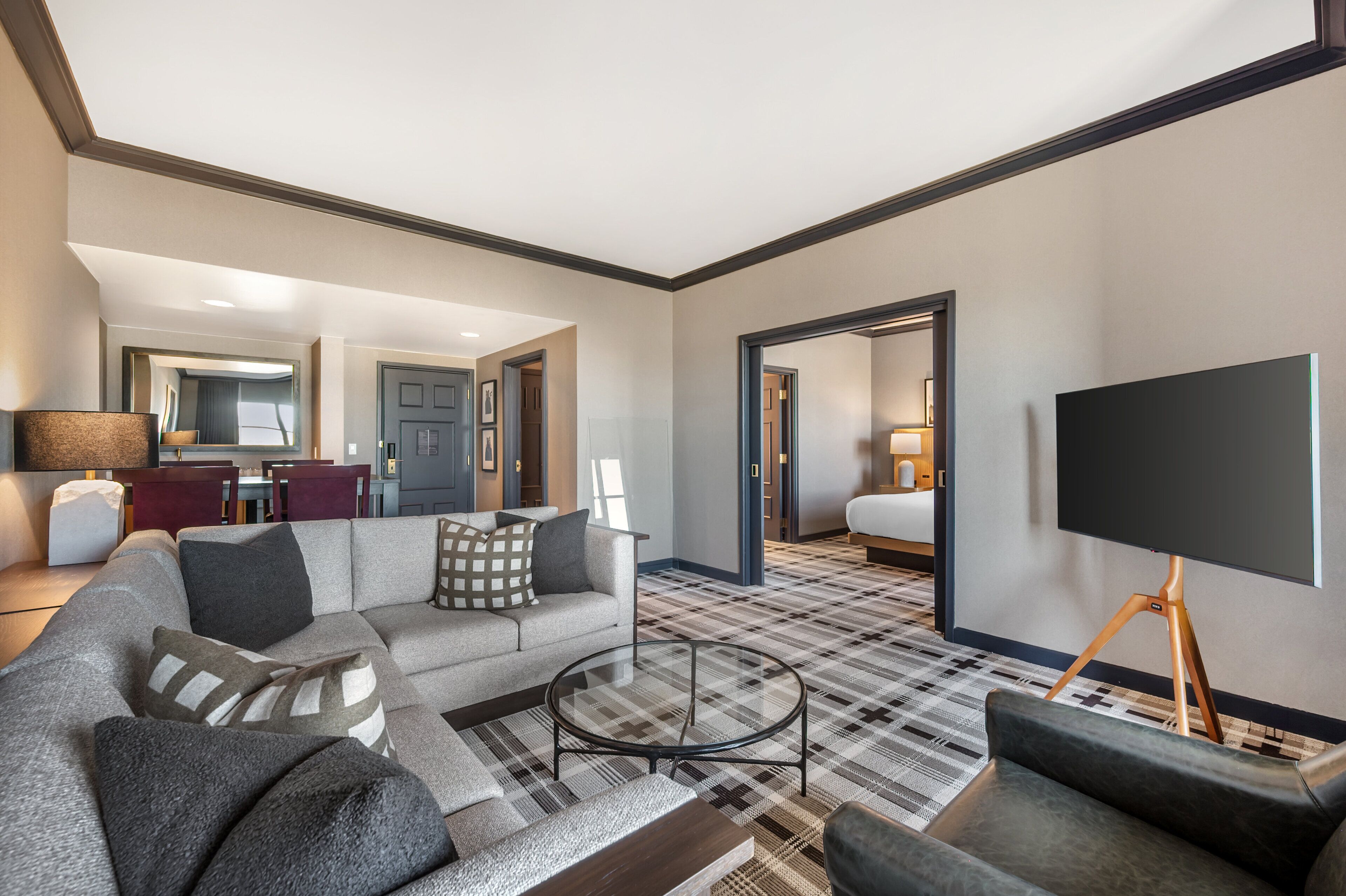A modern hotel room with a large sofa, a coffee table, and a flat-screen TV on a stand.