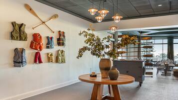 A modern interior with a wall displaying various outdoor gear, a wooden table with a vase and candle, and a view of the city through large windows.