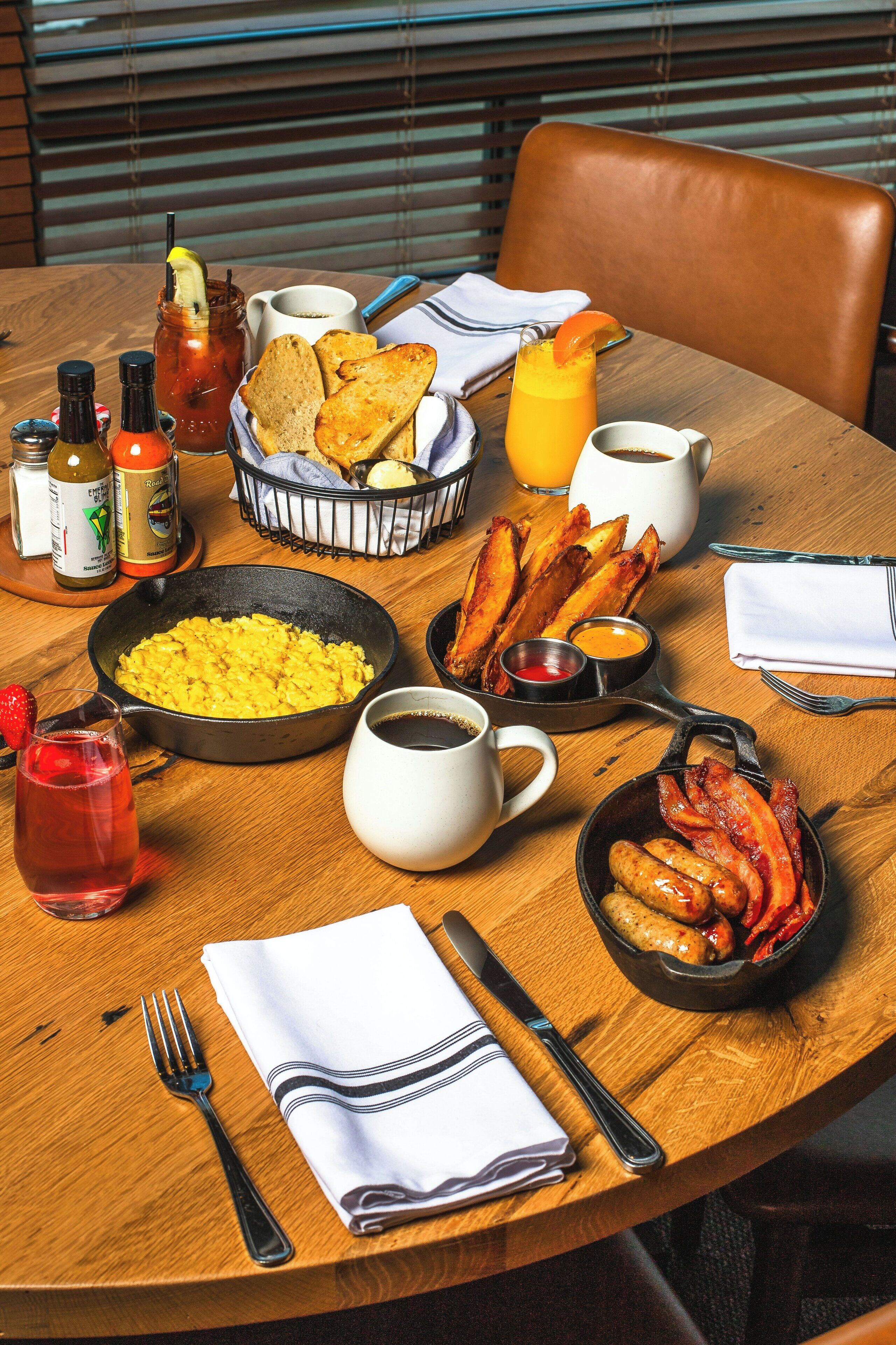 A breakfast table with scrambled eggs, bacon, toast, and beverages.