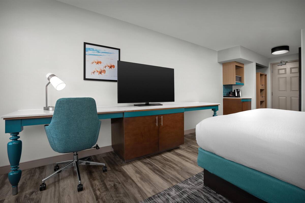 A hotel room with a bed, desk, chair, TV, and a framed picture on the wall.