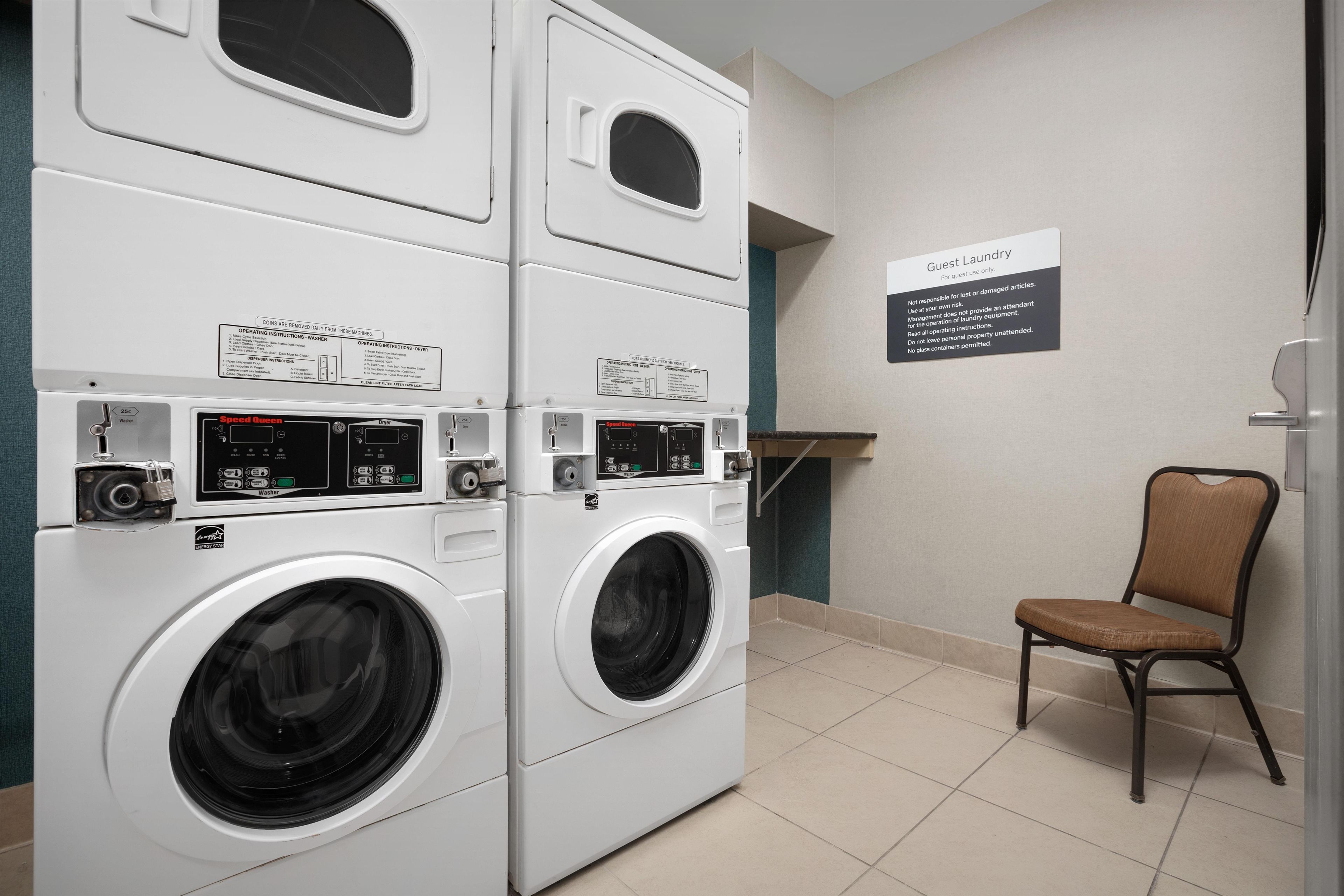 A laundry area with stacked washer and dryer units, a sign indicating guest use, and a chair.