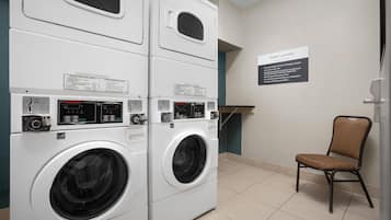 A laundry area with stacked washer and dryer units, a sign indicating guest use, and a chair.