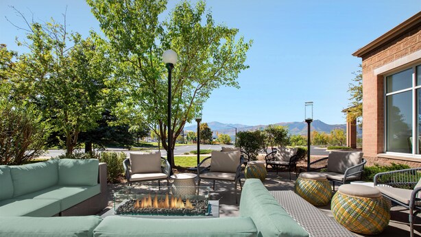 An outdoor seating area with a fire feature, wicker furniture, and a view of mountains. - Hilton Garden Inn Colorado Springs North Air Force Academy (Colorado Springs)