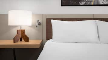 Een hotelkamer met een bed, een nachtkastje met een lamp en een aan de muur hangend schilderij.