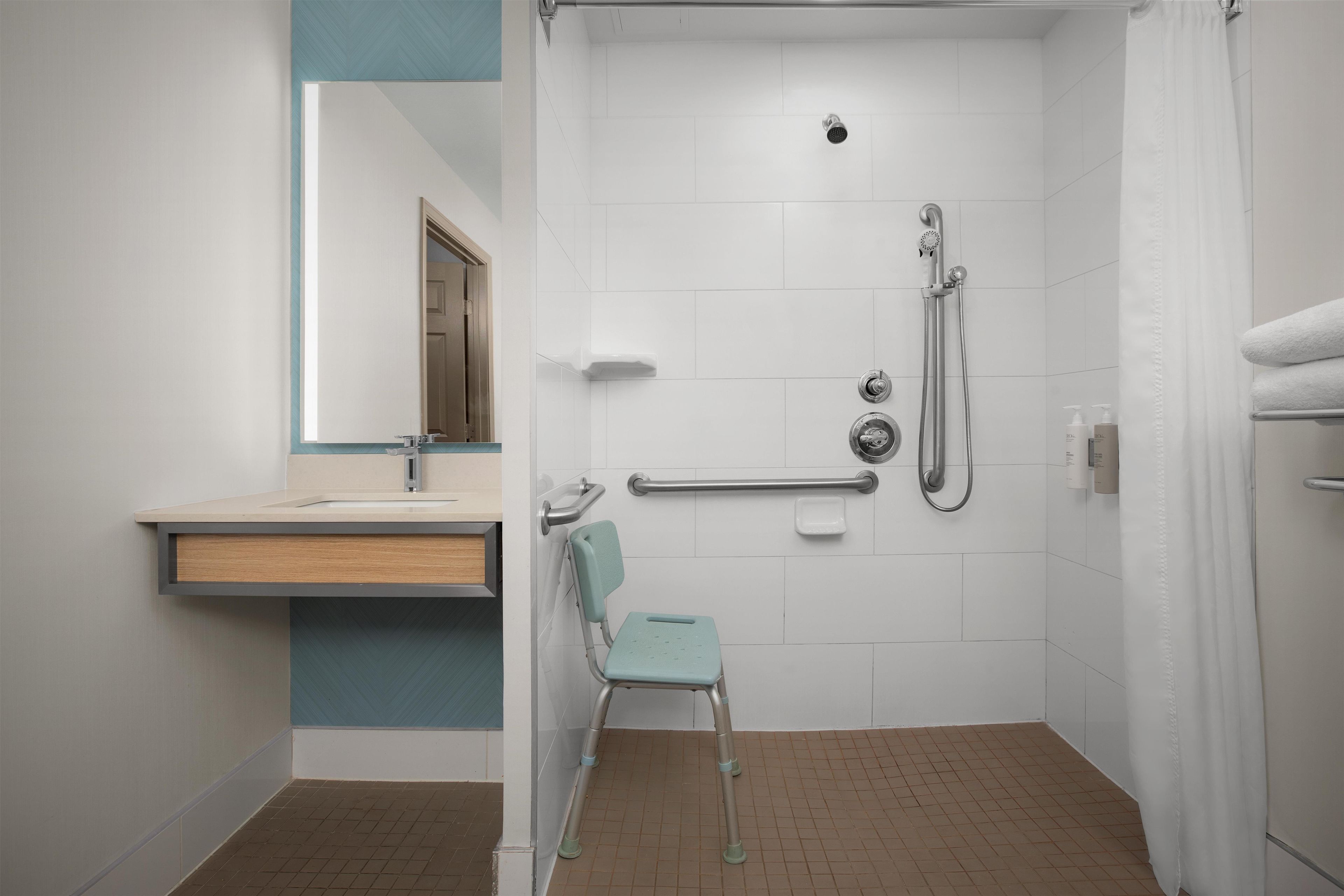 Un baño con ducha, lavamanos y una silla.