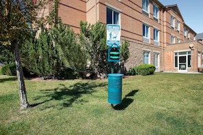 A pet waste station with a sign warning about disease transmission, located in front of a building with a brick facade and windows. - Hilton Garden Inn Colorado Springs North Air Force Academy (Colorado Springs)