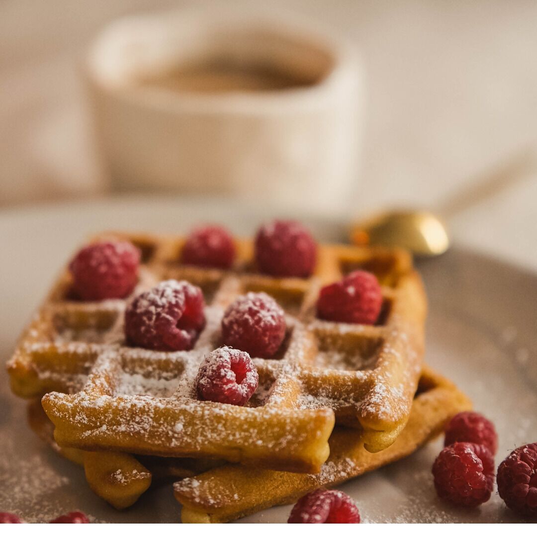 Gros plan d’une gaufre belge recouverte de sucre glace et de framboises.