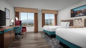 A hotel room with a desk, two beds, a TV, and a large window with a mountain view. - Hilton Garden Inn Colorado Springs North Air Force Academy (Colorado Springs)