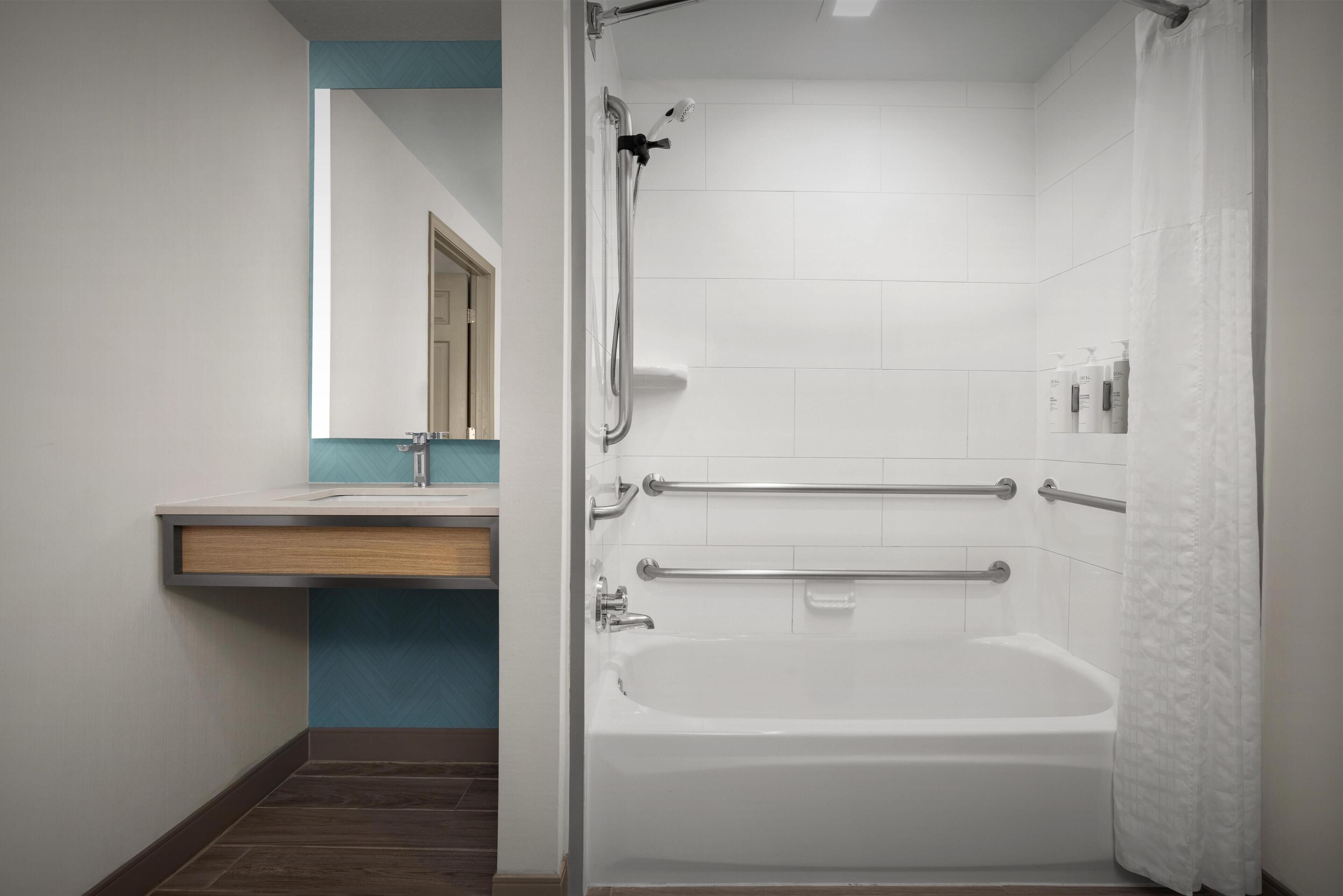 A modern bathroom with a bathtub, a shower, and a handrail.